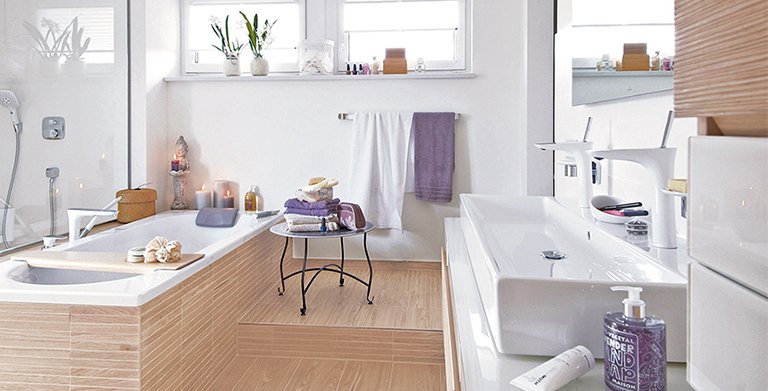 Im Masterbad verbindet ein Podest die Badewanne mit dem Waschtisch. Möbelfronten und Fliesen in Holzoptik verschmelzen zu einem harmonischen Gesamtbild. Copyright: 